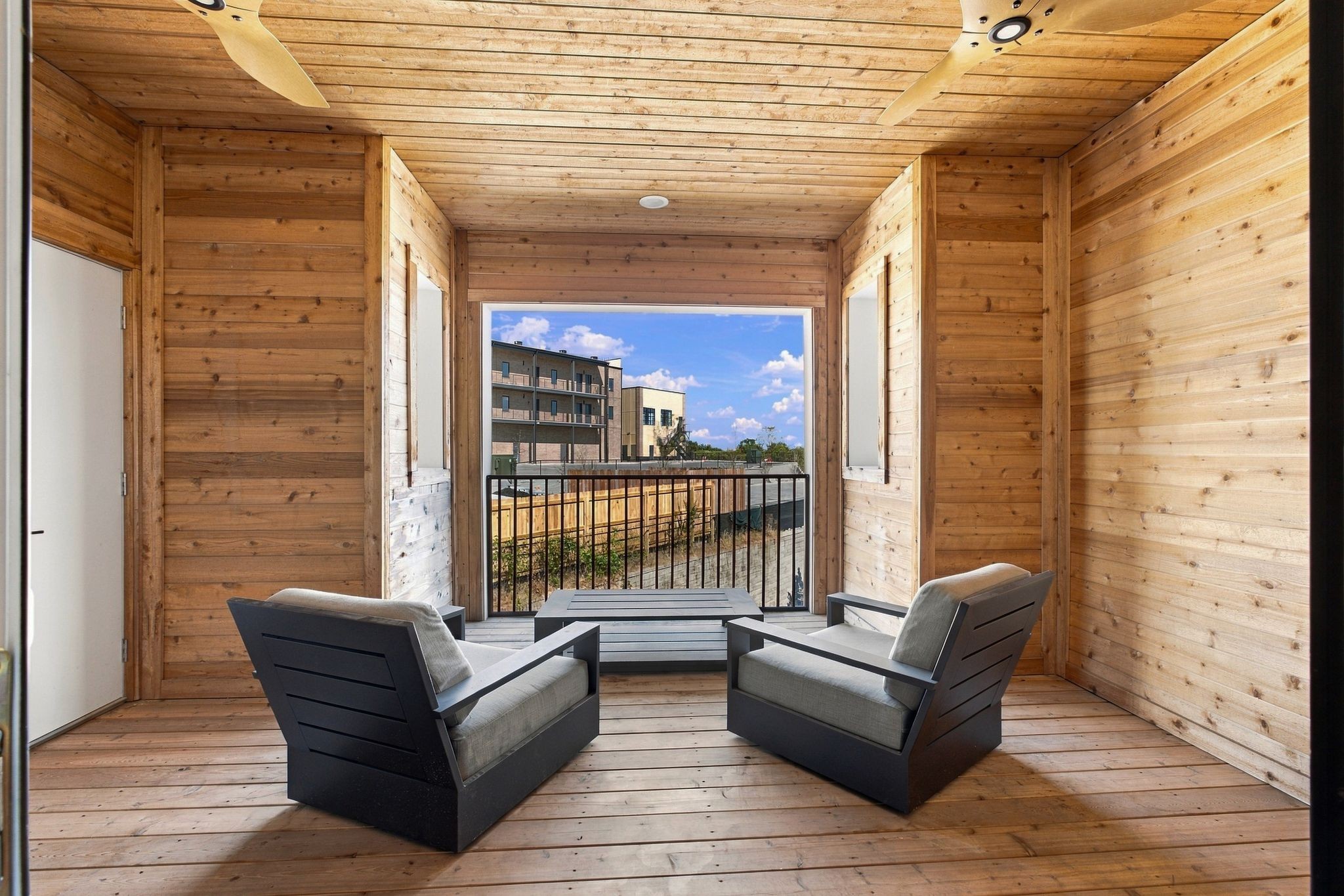 Wood-paneled covered balcony with two lounge chairs and a view of a neighboring apartment building.
