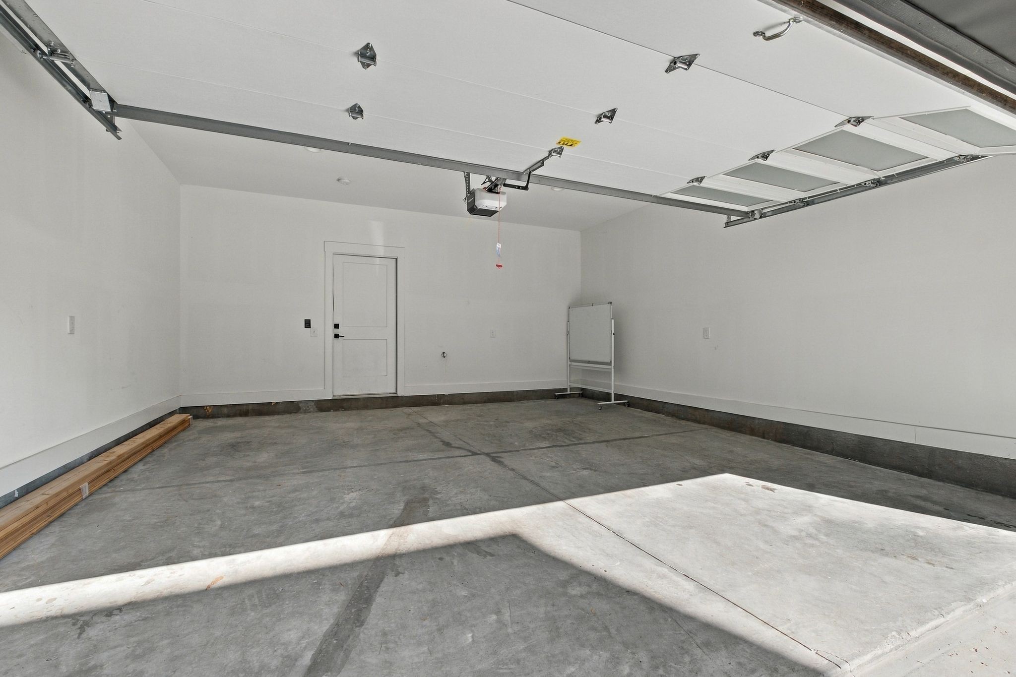 Empty garage with a raised overhead door, concrete floor, and sunlight across the floor.