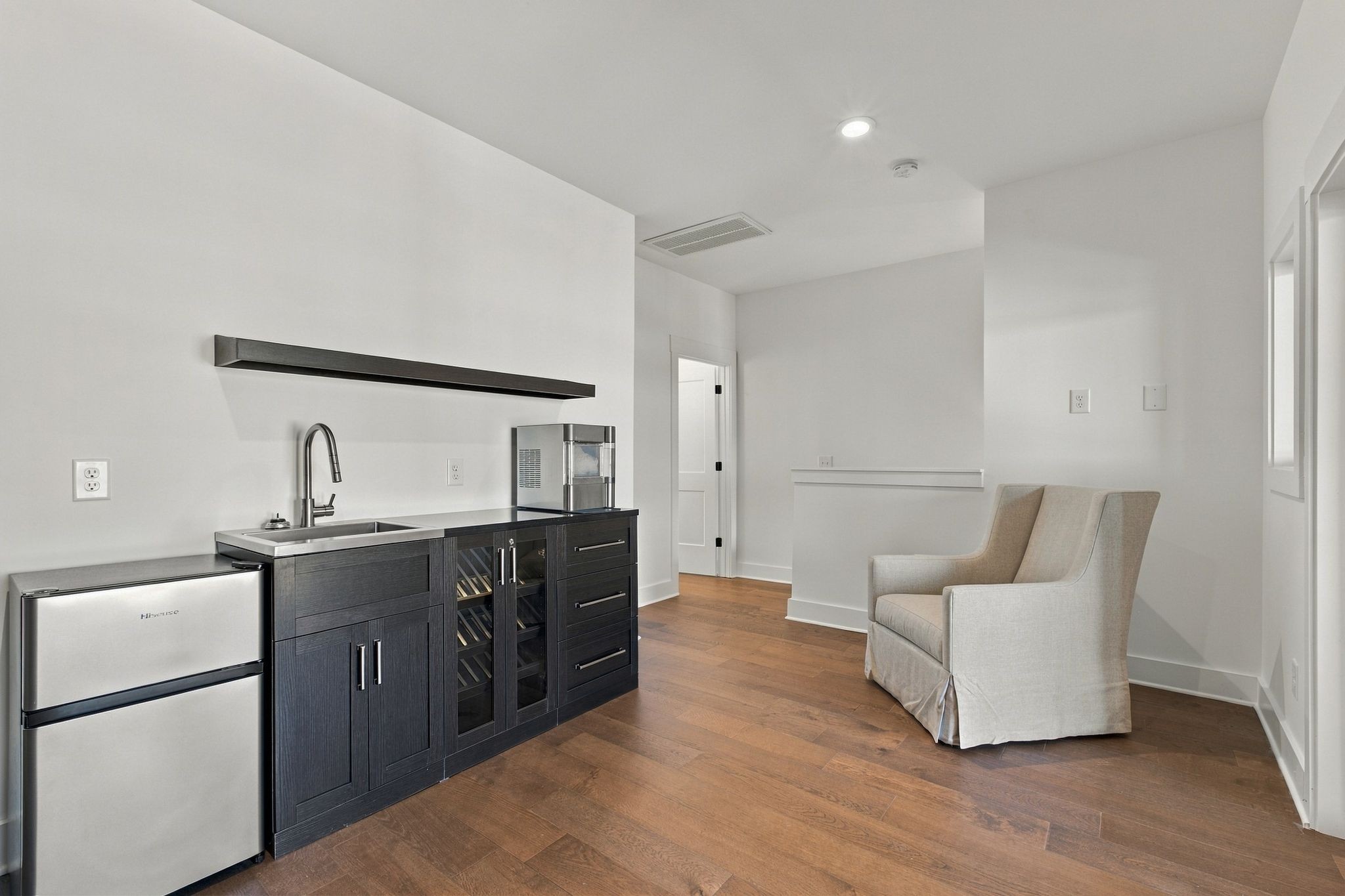 Room with a dark wet bar, stainless mini fridge, wine storage, and two upholstered chairs.