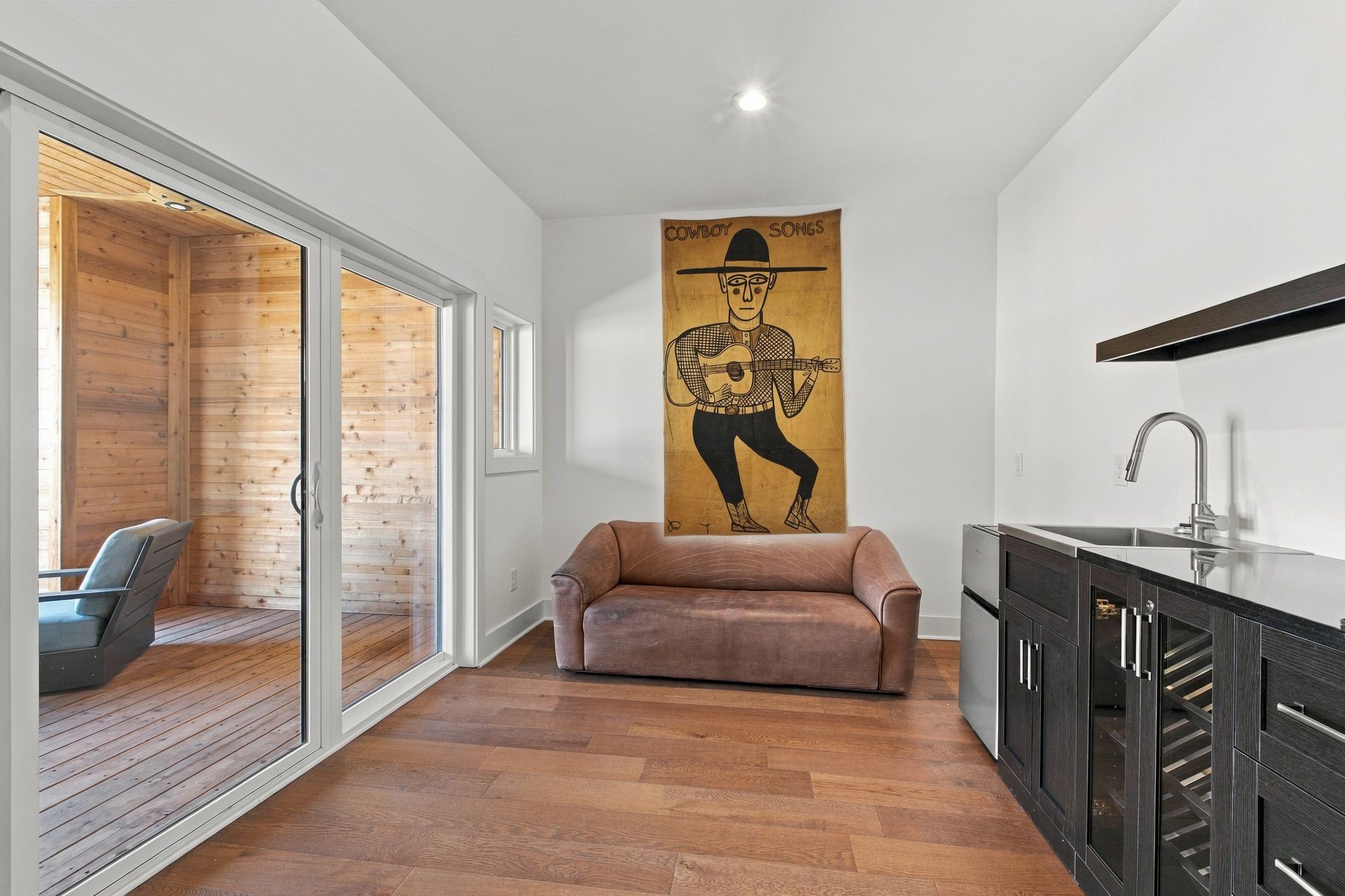 Interior with a loveseat, compact dark kitchenette, and sliding doors to a cedar-lined balcony.