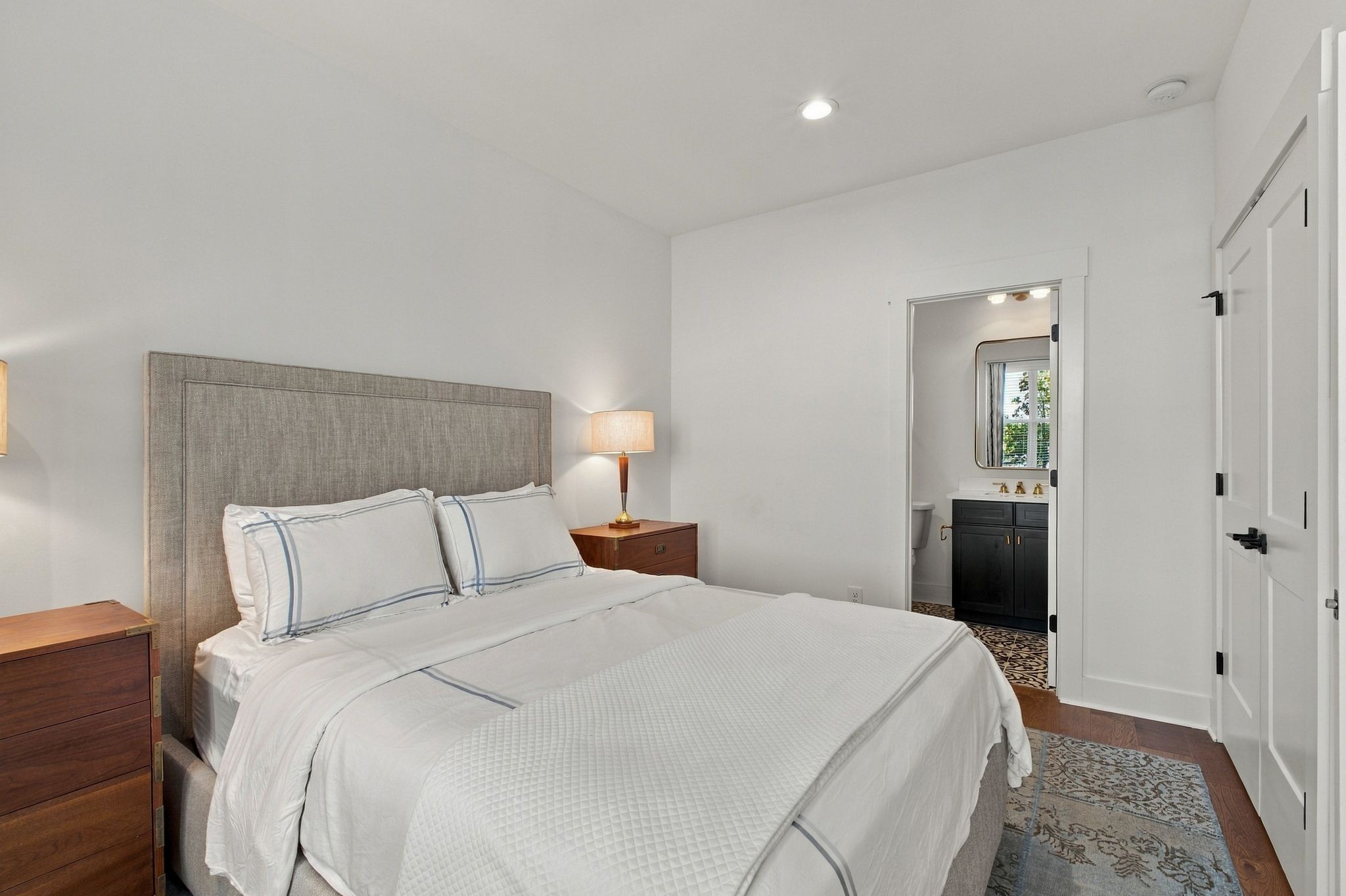 Bedroom with a white bed, tall upholstered headboard, and doorway to an adjoining bathroom.