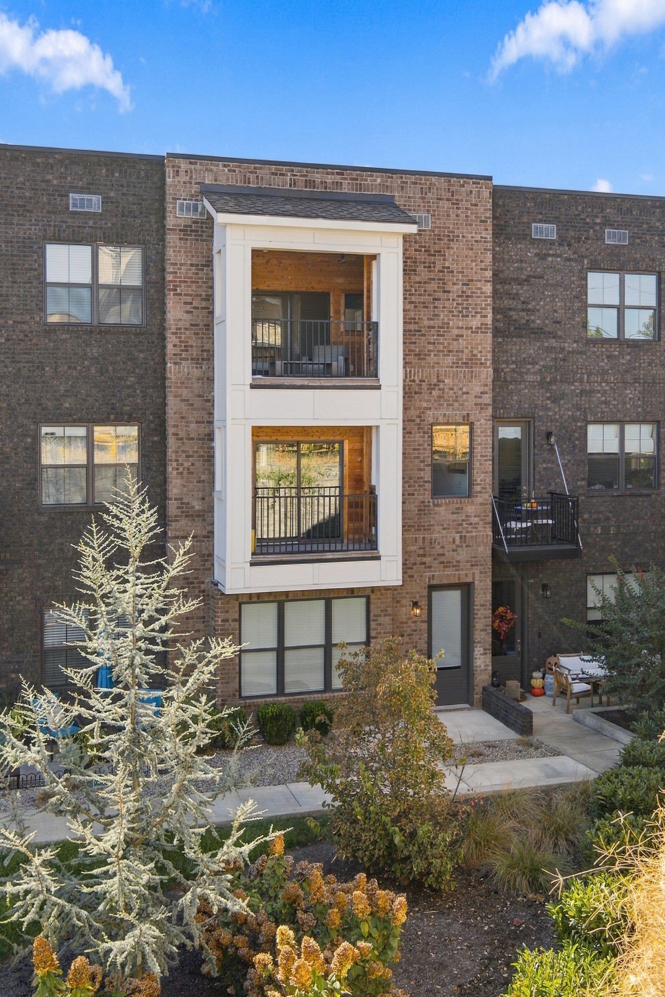 Brick condominium exterior with two stacked balconies and landscaped autumn grounds.