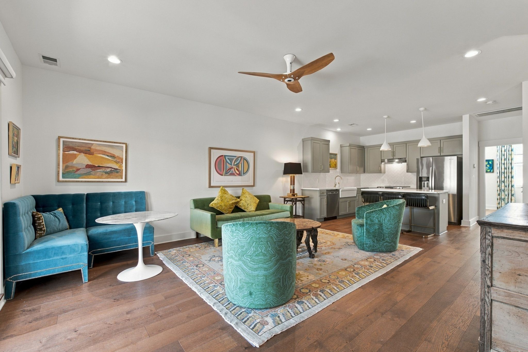 Open-plan living room and kitchen with colorful seating, patterned rug, and stainless steel appliances.