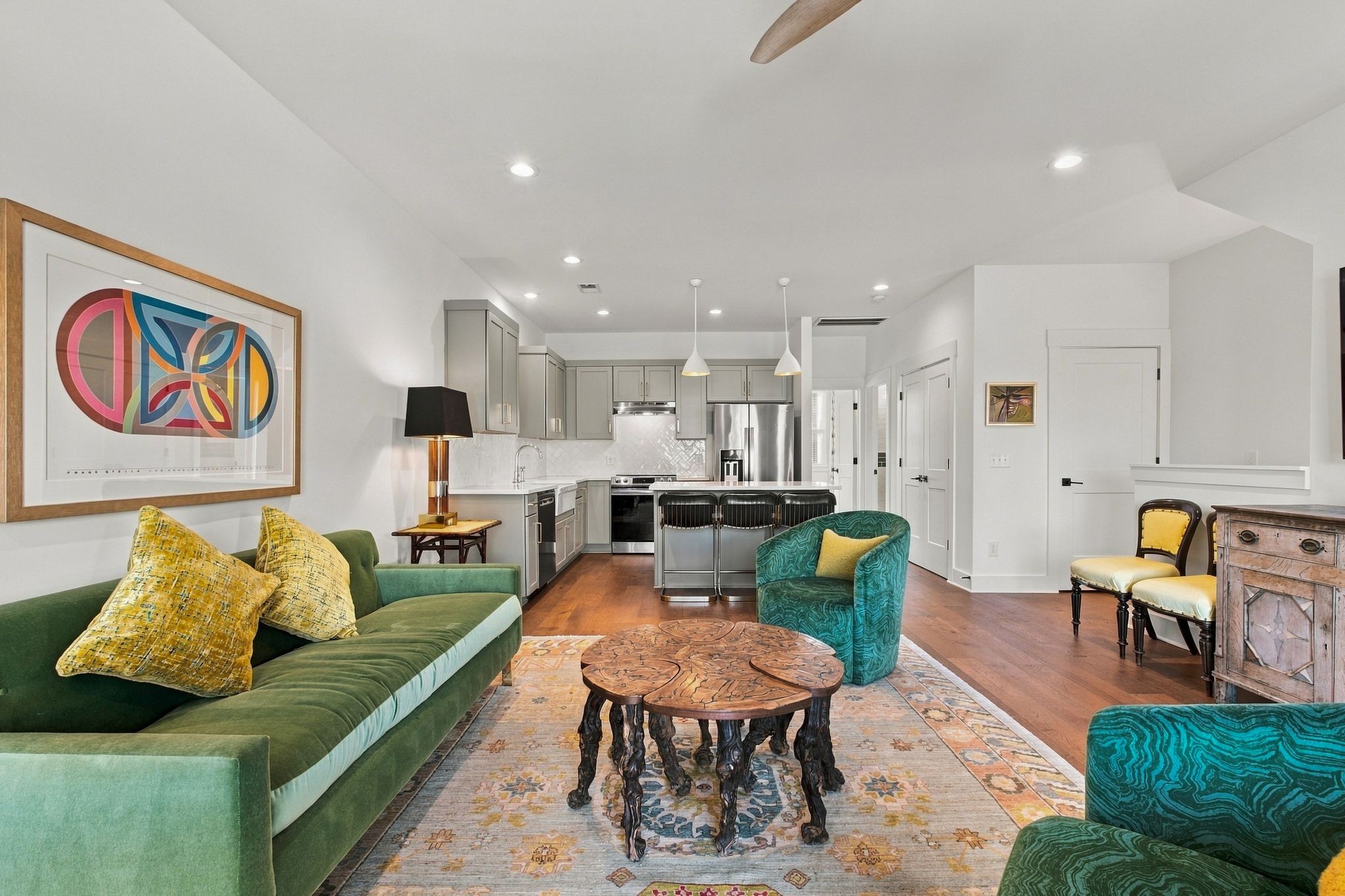 Open-plan living room and kitchen with a green sofa, teal chairs, and gray cabinets.