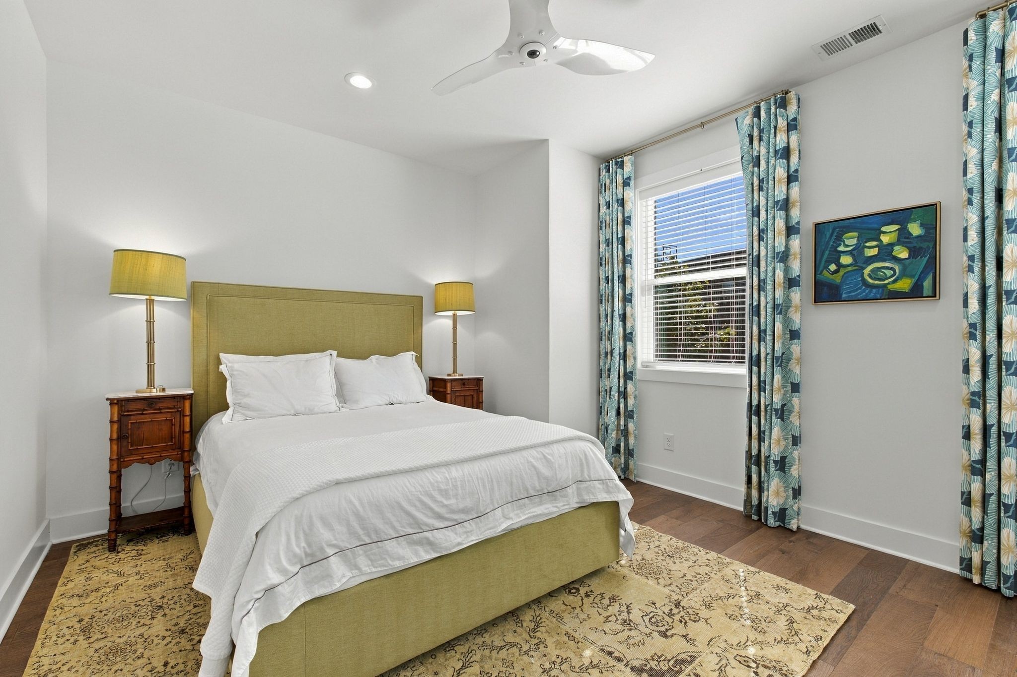 Bedroom with an olive-green bed, blue patterned curtains, and a large rug.