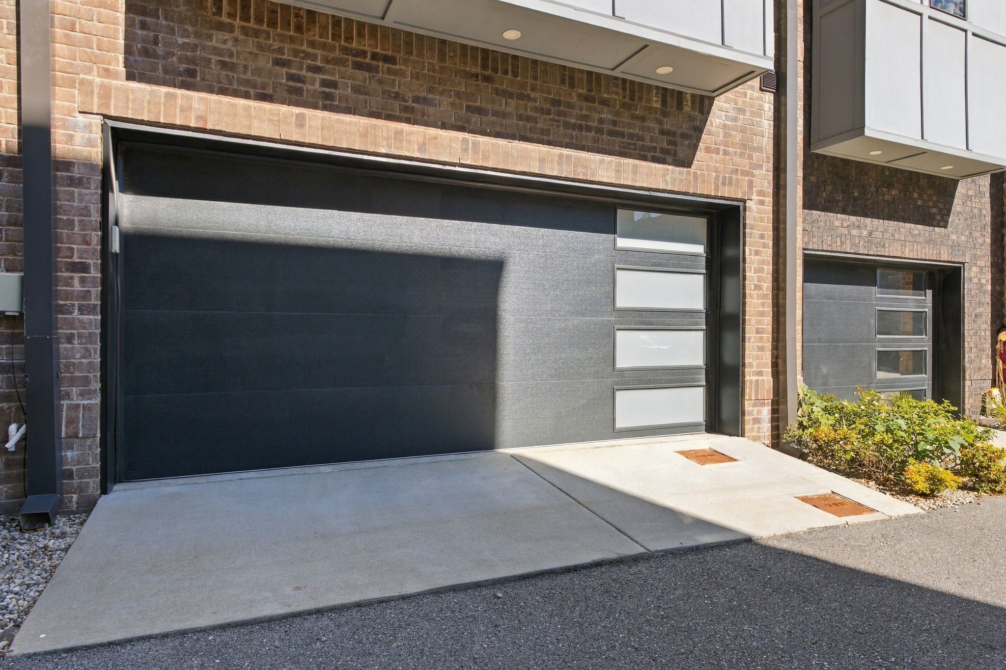 Brick townhome with a dark modern garage door and concrete driveway.