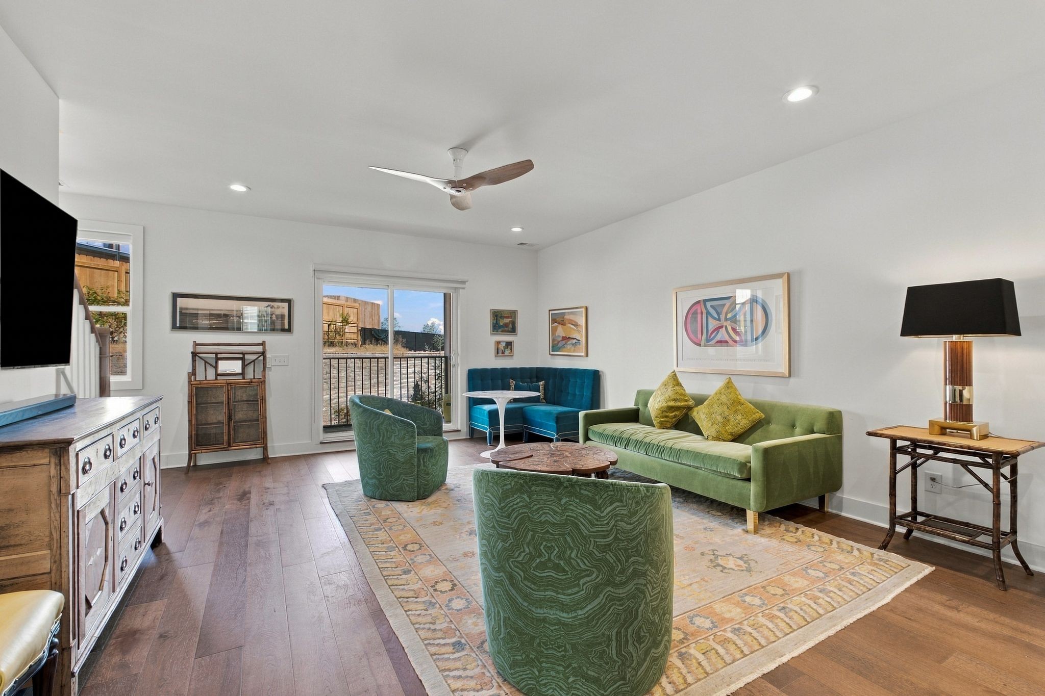 Living room with green seating, a blue banquette, patterned rug, and sliding doors to a balcony.