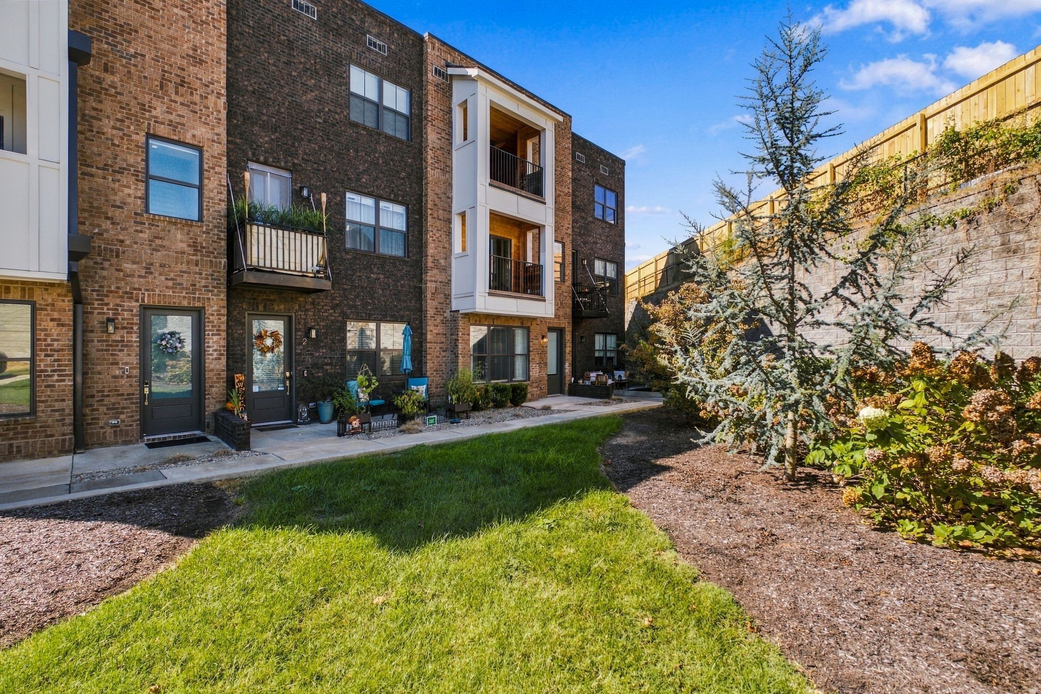 Brick residential building with balconies and patios beside a landscaped courtyard.