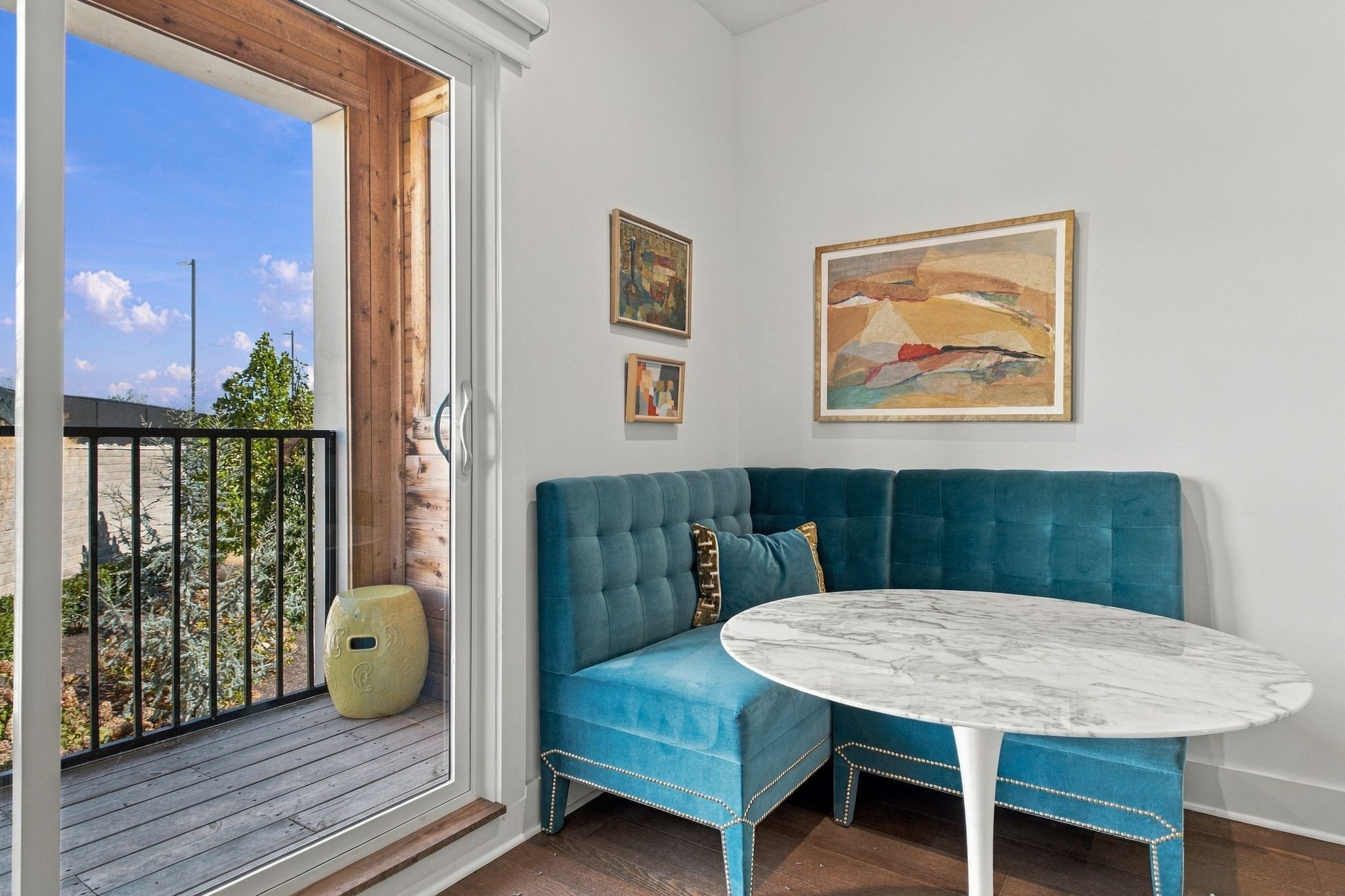 Dining nook with a teal banquette and oval table beside a sliding door to a small balcony.