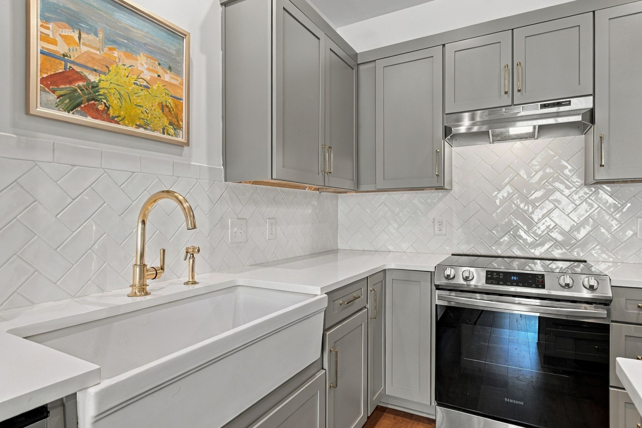 Kitchen with gray cabinets, white tile backsplash, farmhouse sink, brass faucet, and stainless range.