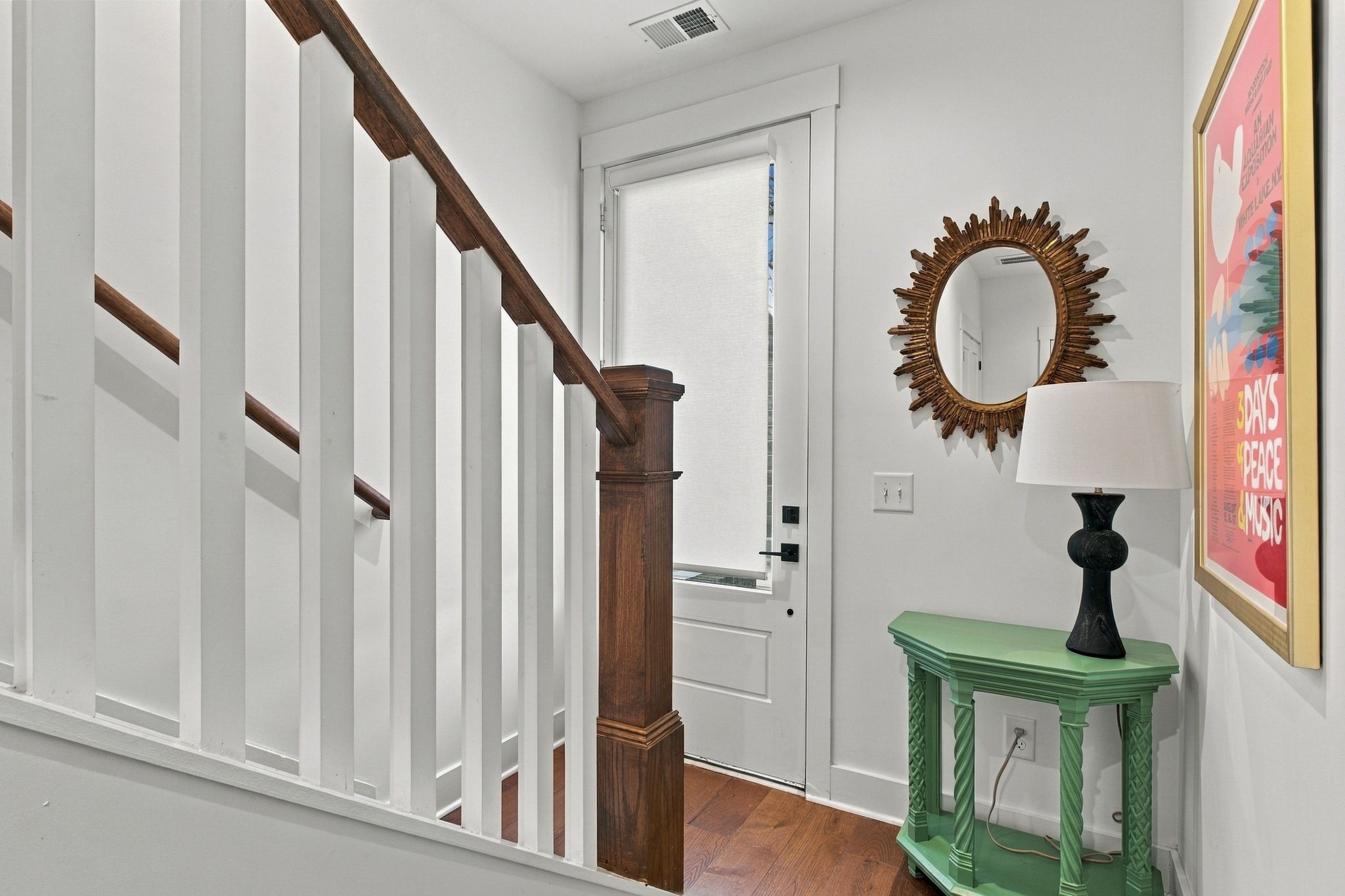 Entryway with a white staircase, dark wood railing, and green console table beneath a sunburst mirror.