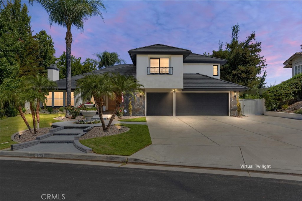 Two-story home with stone accents, a two-car garage, and palm trees in the front yard at dusk.