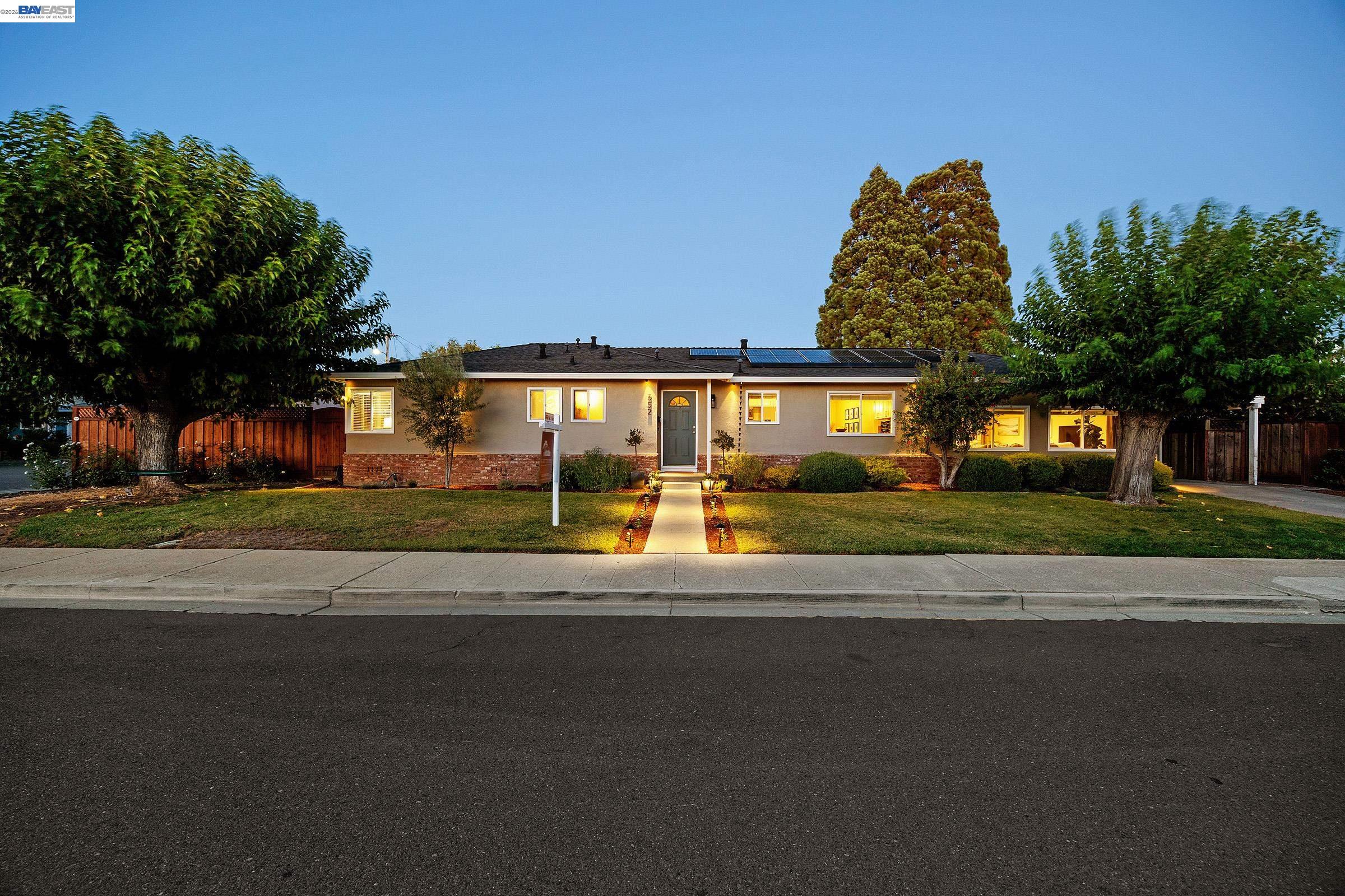 Single-story home at dusk with rooftop solar panels and an illuminated front walkway.