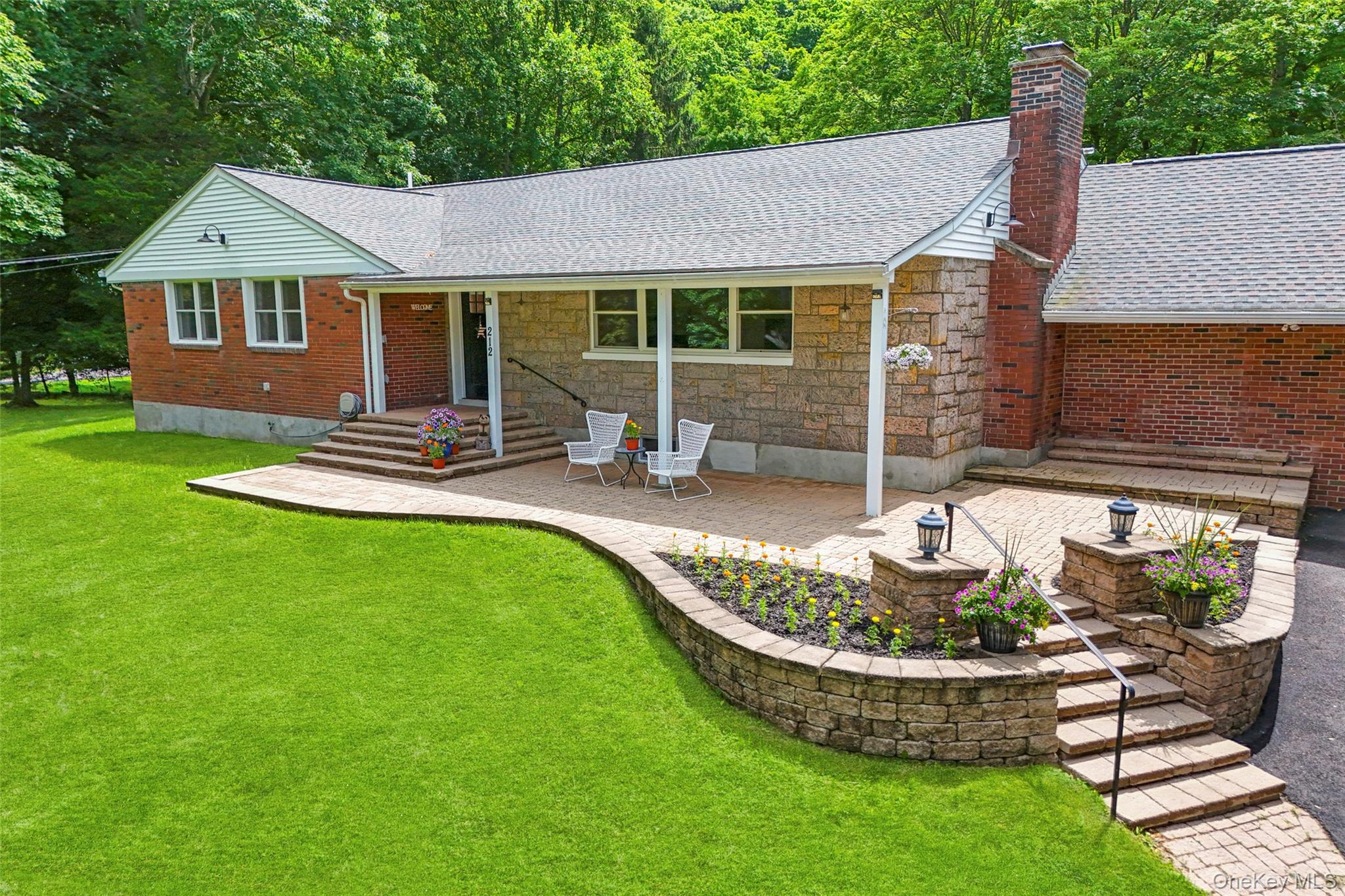 Single-story brick and stone home with a covered patio, landscaped garden, and broad green lawn.