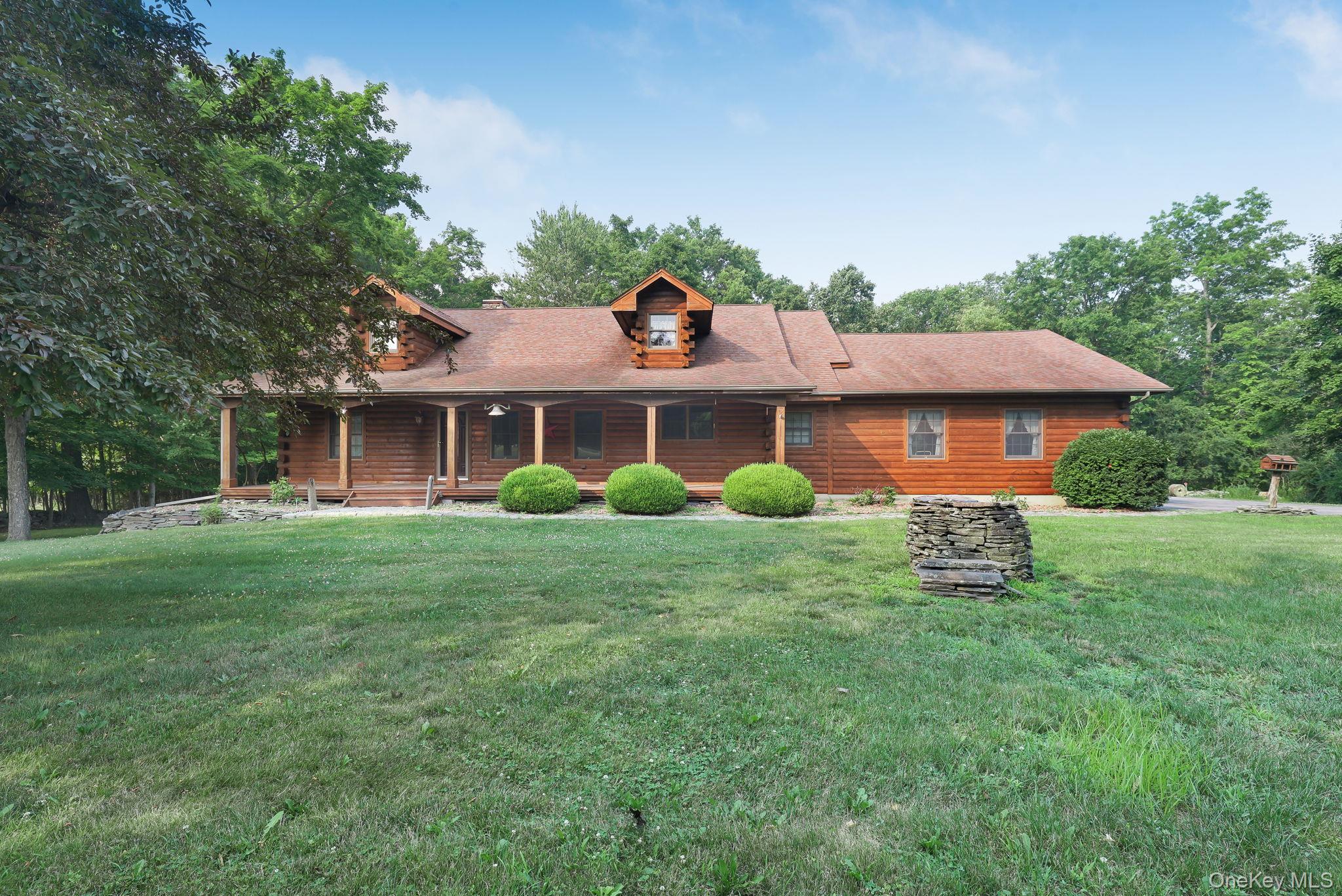 Log cabin-style home with a covered porch, roof dormers, and a broad green lawn.