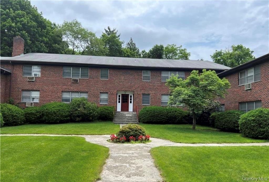 Two-story brick apartment building with a central entrance and a flower garden beside the walkway.
