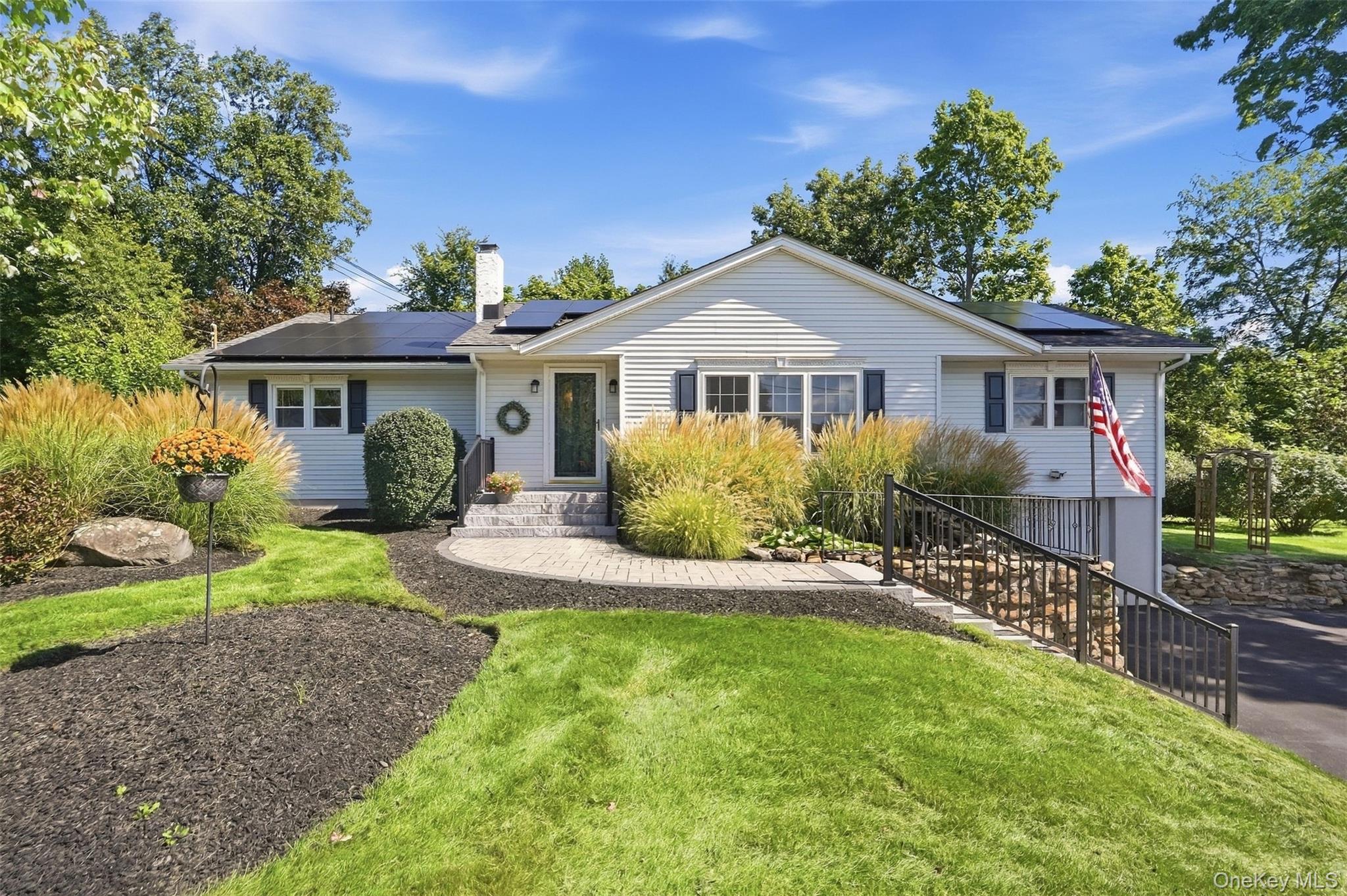 White single-story home with rooftop solar panels, landscaped front yard, and an accessibility ramp.