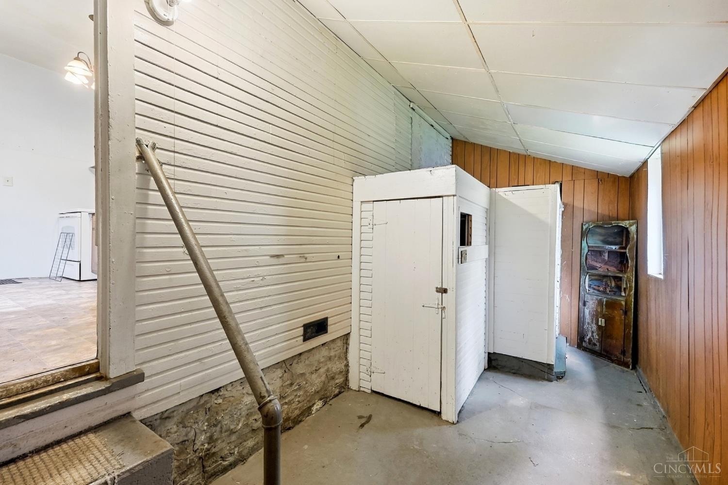 Basement passage with white storage enclosures, a concrete floor, and wood-paneled walls.
