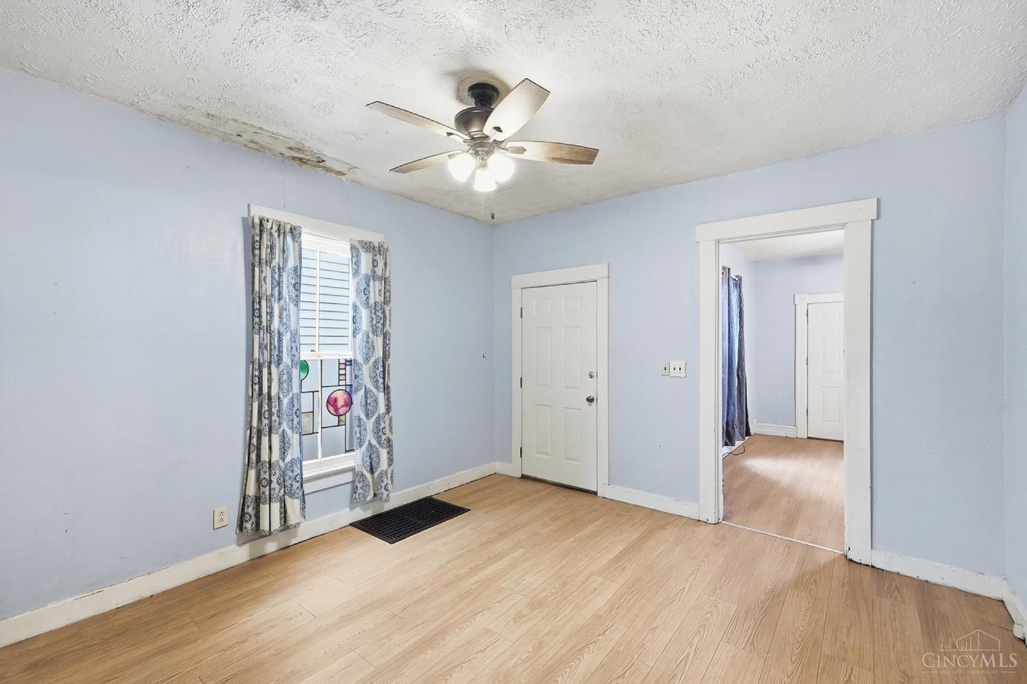 Vacant room with light wood flooring, a ceiling fan, and a stained ceiling.