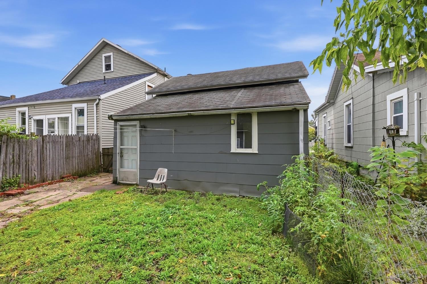 Gray detached garage at the back of a grassy yard, with a concrete walkway and chain-link fence.