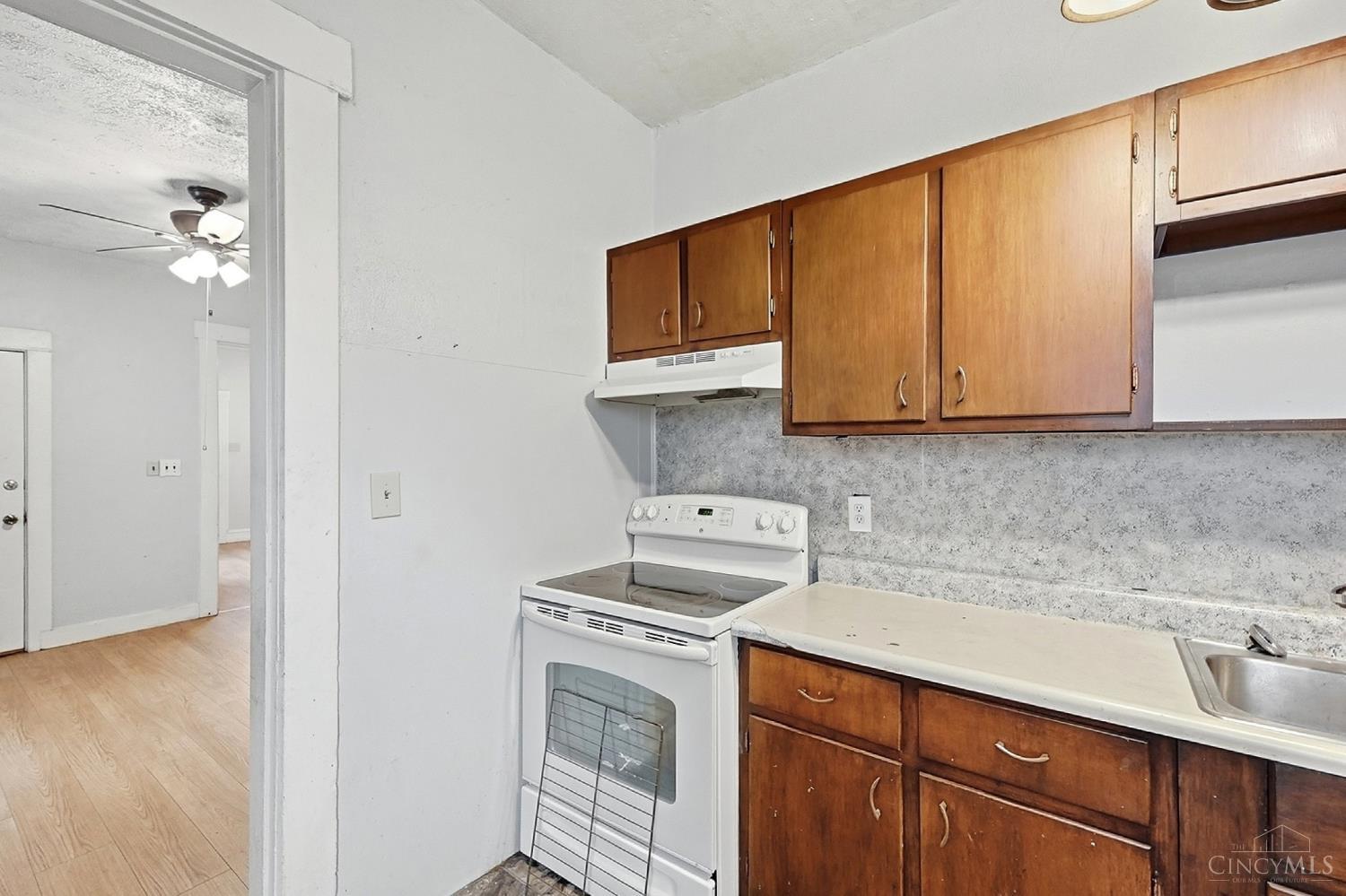 Kitchen with honey-brown cabinets, a white electric range, and a stainless-steel sink.