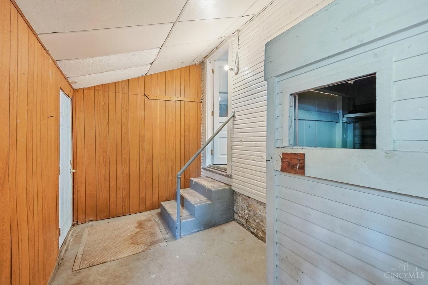 Covered entry with wood-paneled walls, blue steps and railing, and a white door.