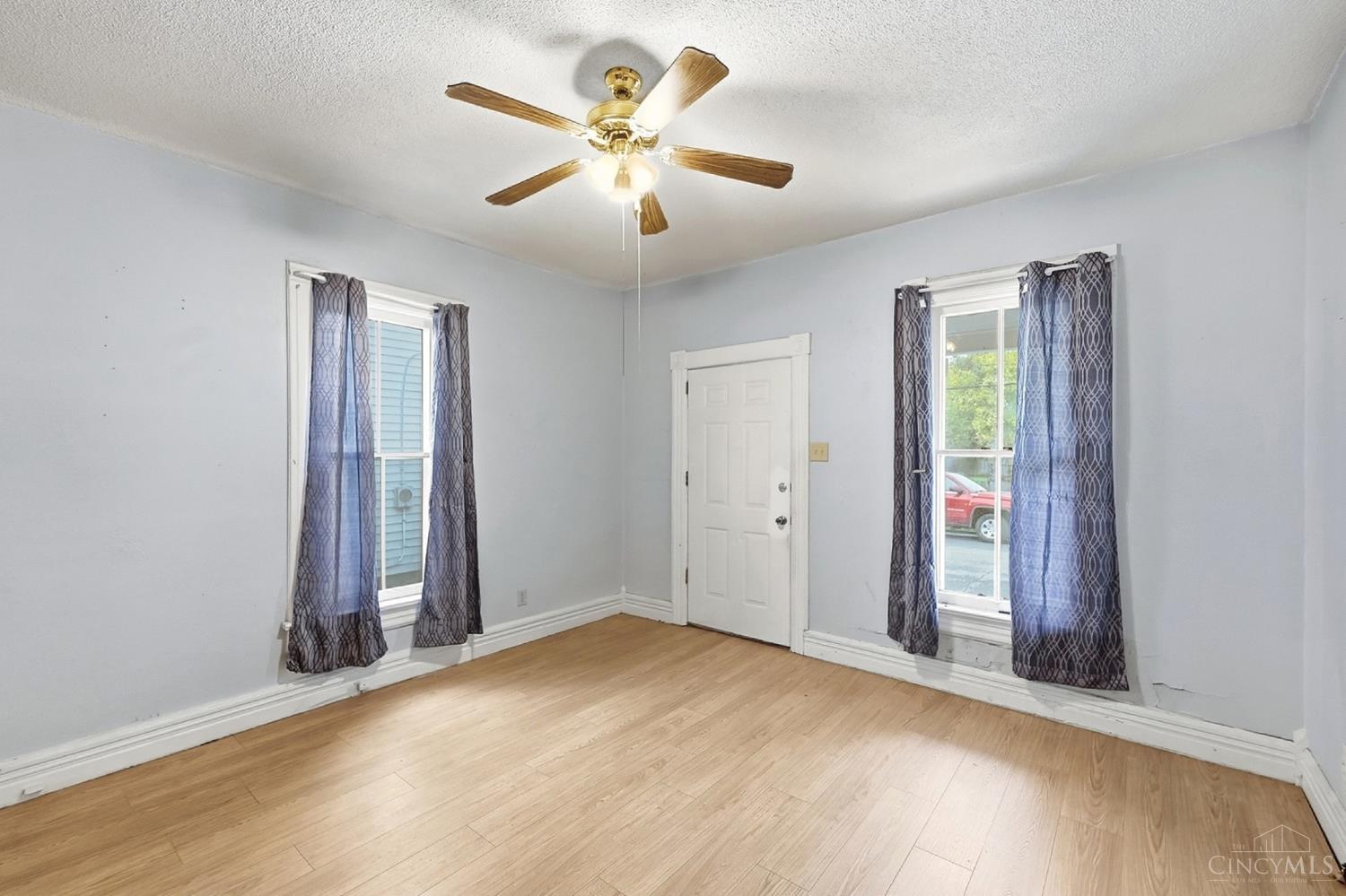 Empty room with light wood flooring, two curtained windows, and a ceiling fan.
