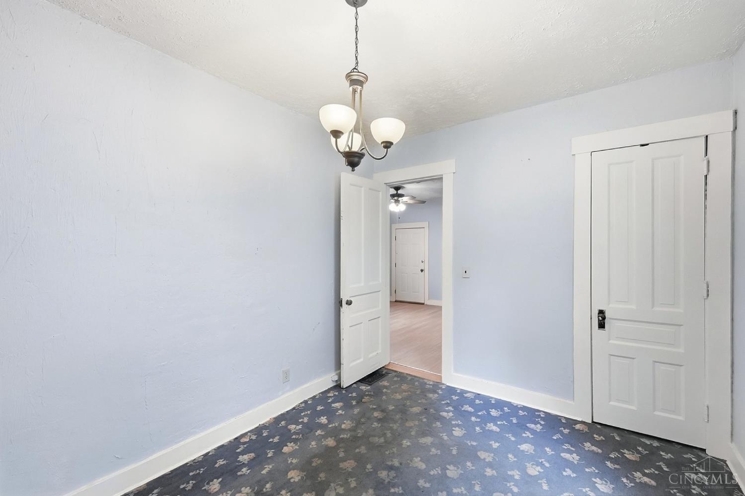 Empty bedroom with floral carpet, pale blue walls, chandelier, and white paneled doors.