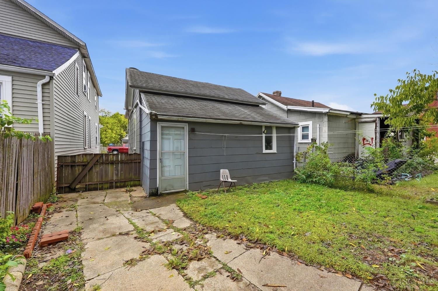 Rear of a gray house with a white door, concrete patio, and grassy yard.