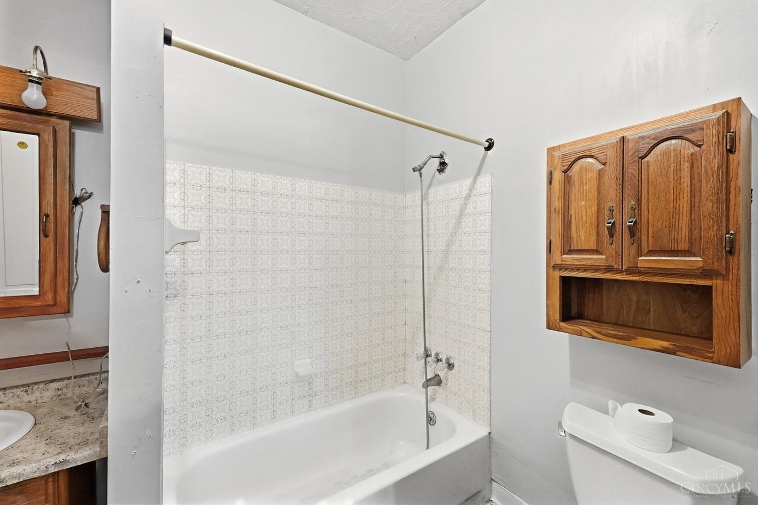 Bathroom with a white tub, patterned tile surround, wooden cabinets, and granite vanity.