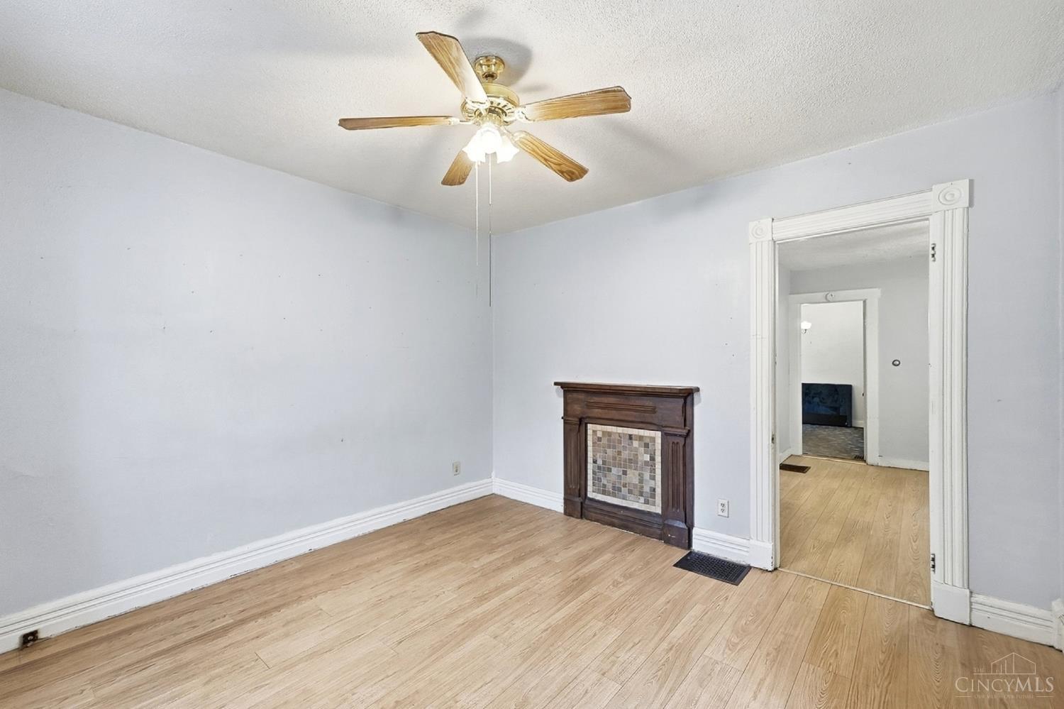 Empty room with light wood flooring, a decorative fireplace, and a ceiling fan with a light.