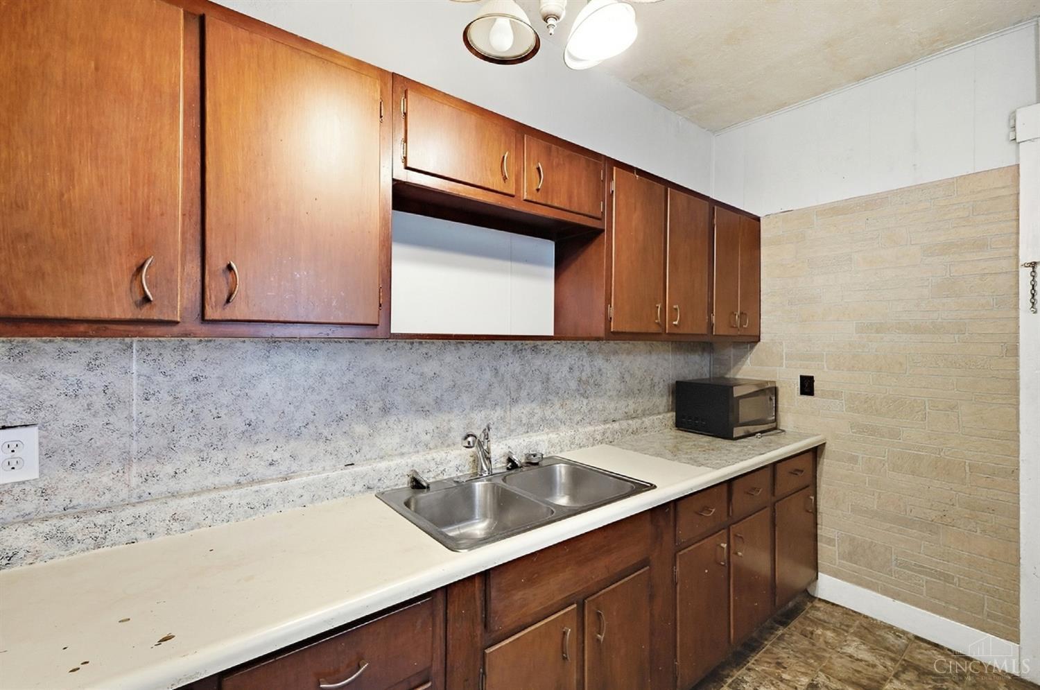 Kitchen with dark wood cabinets, a long counter, and a stainless-steel double-basin sink.