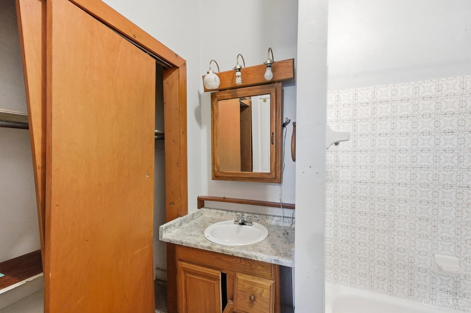 Bathroom with a wooden vanity, framed mirror, and patterned tile around the tub or shower.