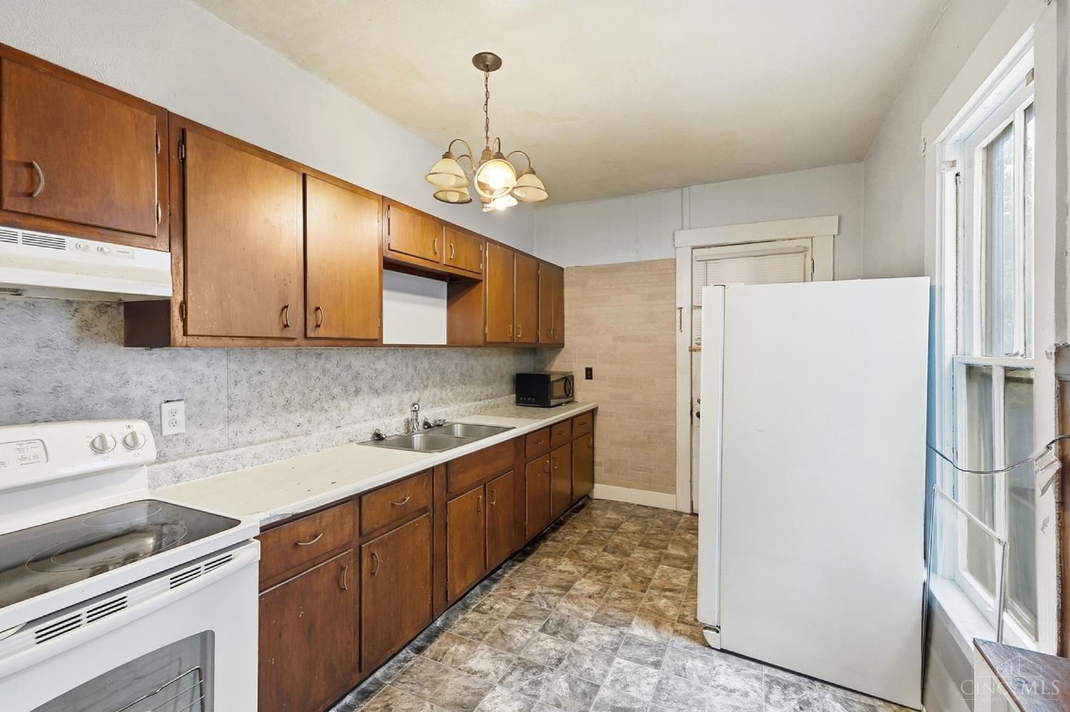 Kitchen with wood cabinets, white appliances, a double-basin sink, and a large window.