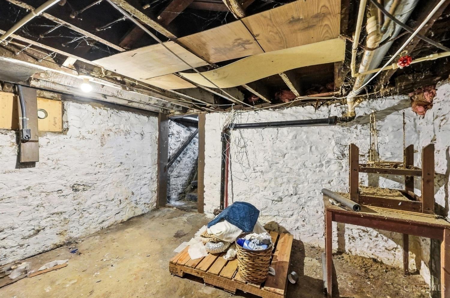 Unfinished basement with stone walls, exposed ceiling utilities, and stored materials.