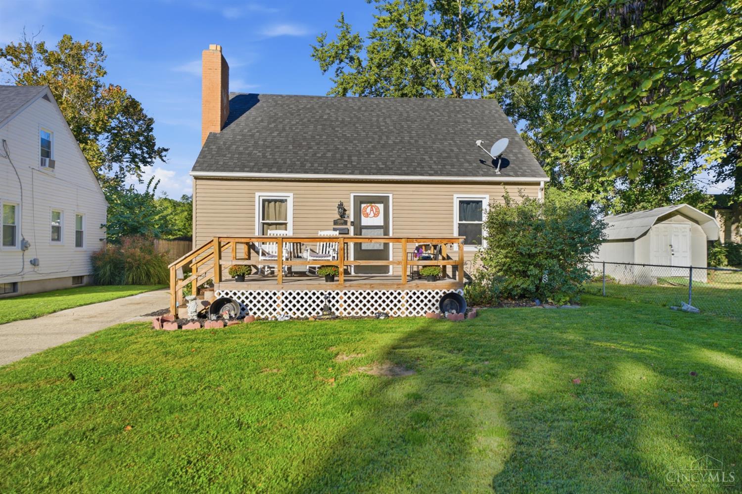 Rear of a beige house with a raised wooden deck, patio furniture, and a broad green lawn.