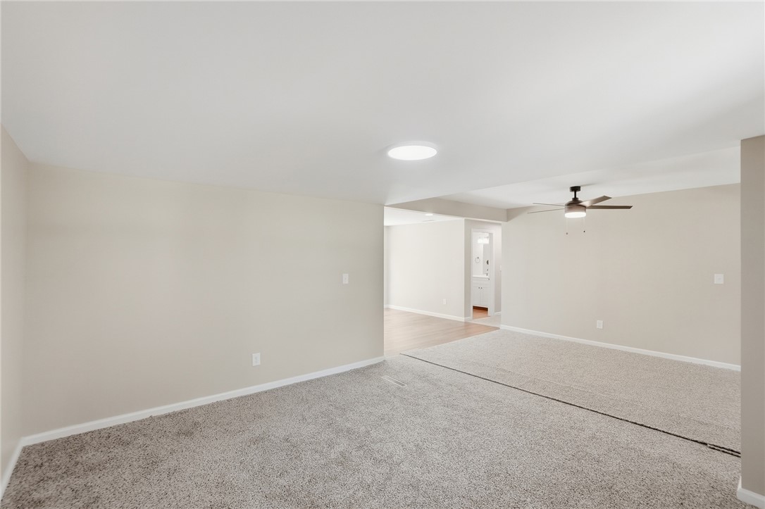 Empty carpeted living area with a ceiling fan and an opening to an adjoining room.