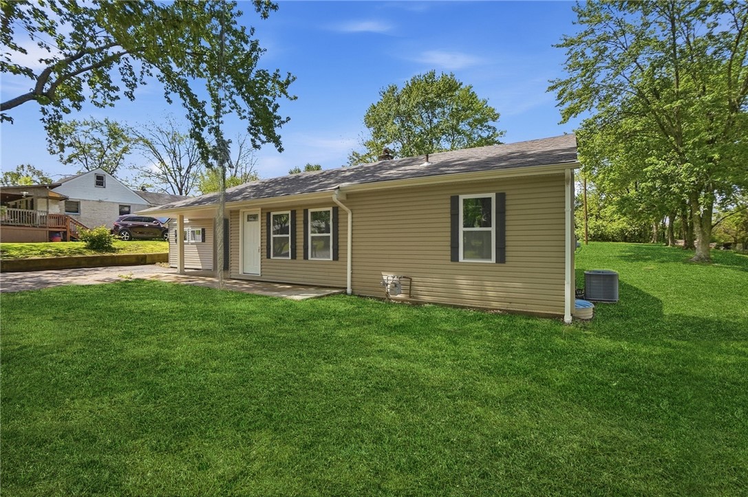 Tan ranch house with dark shutters and a broad green lawn.