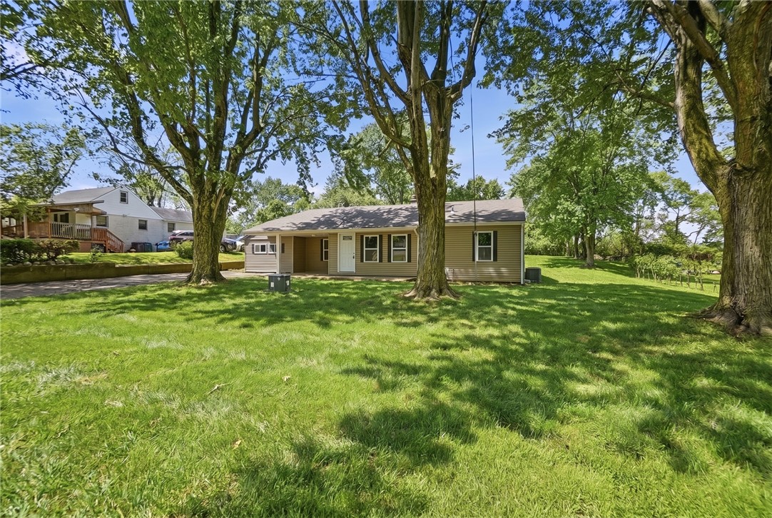Tan ranch house behind a broad, tree-shaded lawn.