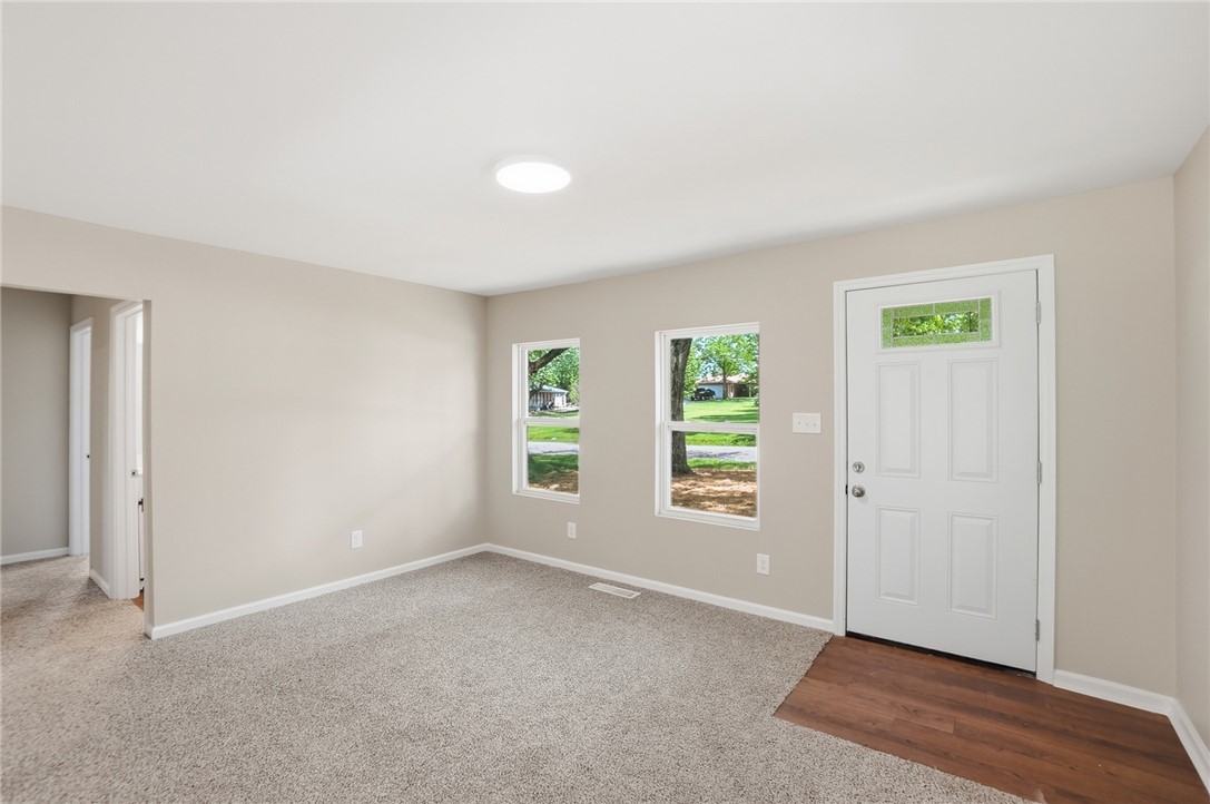 Empty front entry with a white door, two lawn-facing windows, and carpet beside dark wood flooring.
