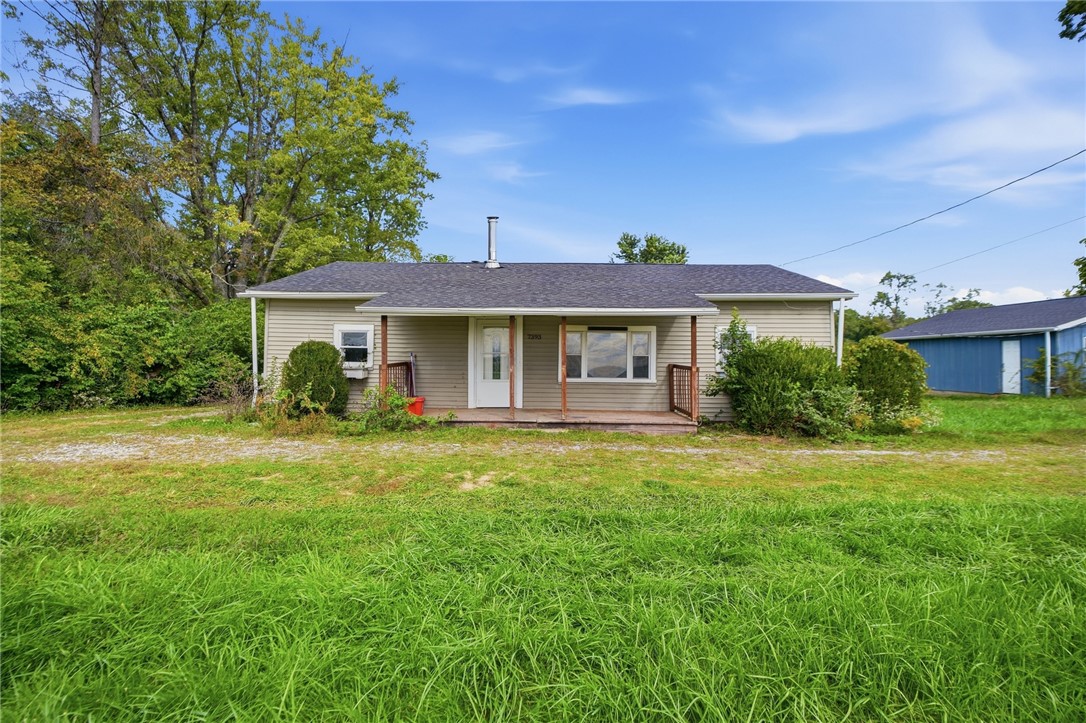 Single-story beige house with a covered porch, window air conditioner, and grassy front lawn.