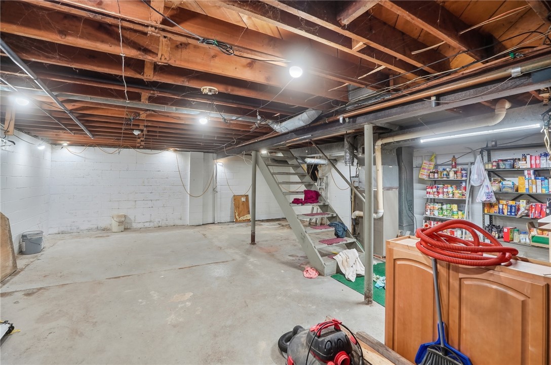 Unfinished basement with exposed joists, concrete floor, stairs, and storage shelves.