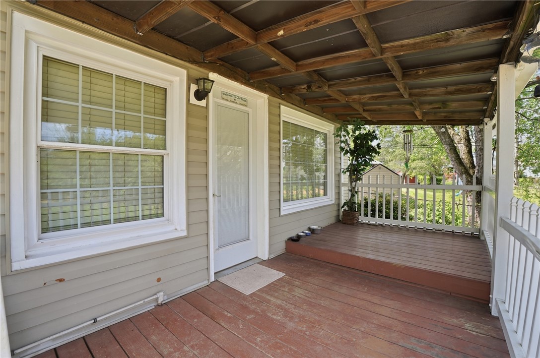 Covered front porch with exposed wood ceiling beams, reddish decking, and white railings.