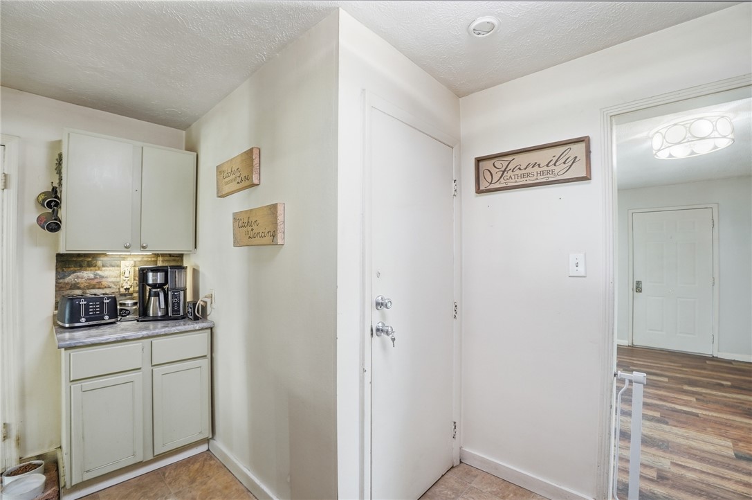 Compact kitchen nook with pale cabinets, countertop appliances, and an entry door beside a family sign.
