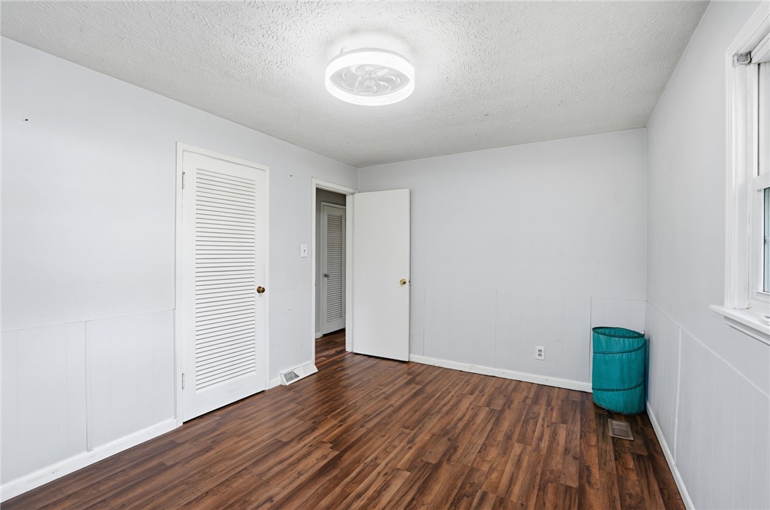 Empty bedroom with wood-look flooring, a louvered closet door, and a window.