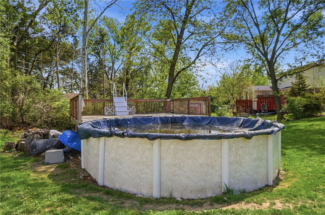 Above-ground backyard pool beside a raised wooden deck, surrounded by mature trees.