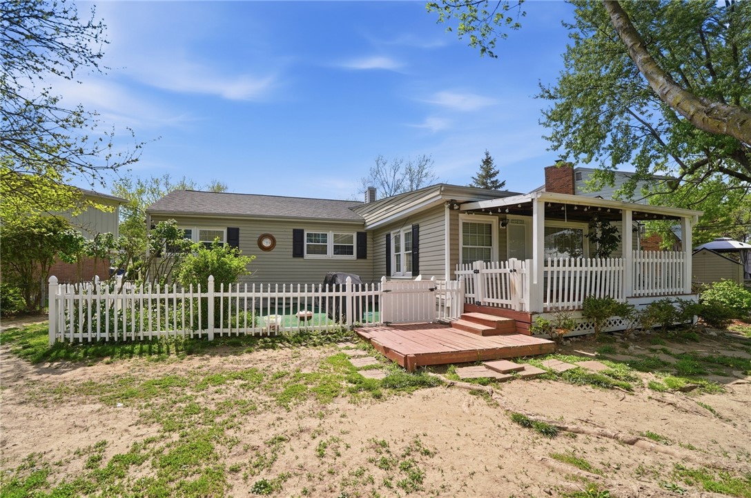 Rear of a beige house with a covered porch, wooden deck, and white picket fence.