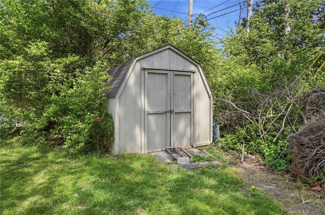 Light gray backyard storage shed with double doors, surrounded by trees and shrubs.