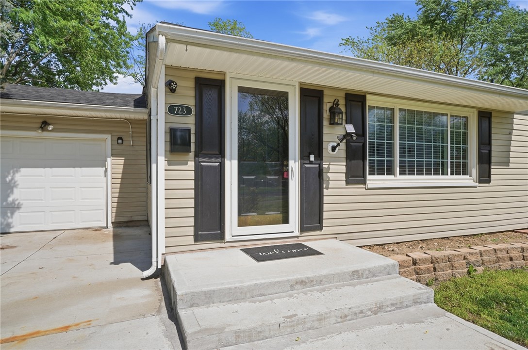 Single-story ranch house with beige siding, dark shutters, attached garage, and concrete front steps.