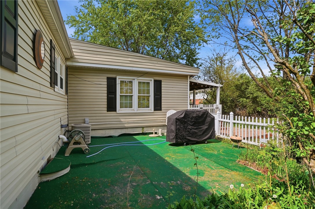 Home patio with green artificial turf, a covered grill, and white picket fencing.